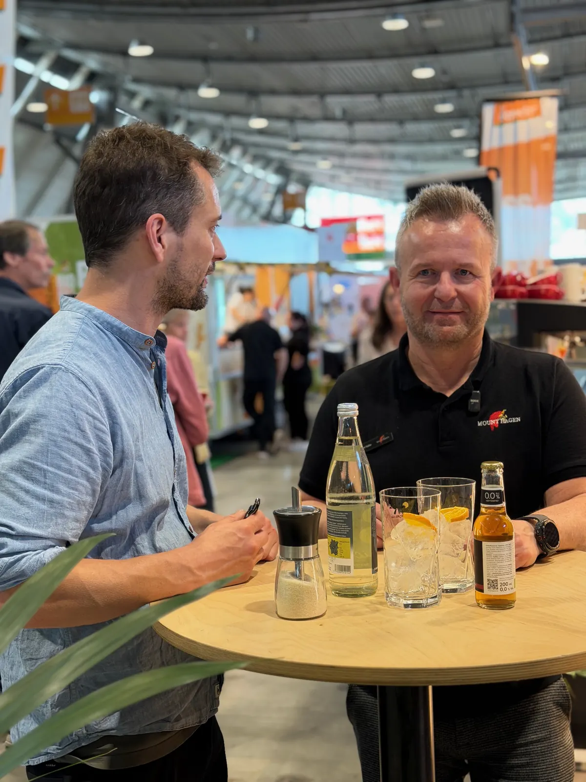 Johannes Schubert von Sankt Sprizz und Farid Keller von Mount Hagen an einem Stehtisch auf einer Messe, auf dem Tisch eine Tonic-Flasche und Gläser mit Eis und getrockneter Orangenscheibe