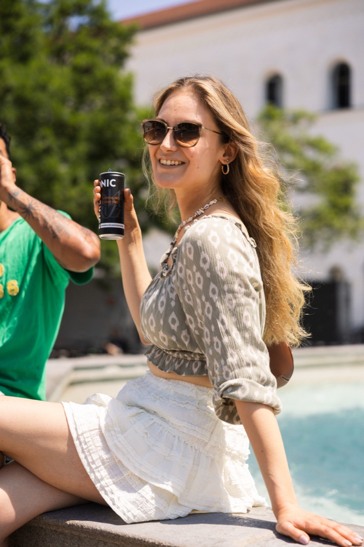 Junge Frau mit Sonnenbrille hält eine Dose Espresso Tonic in die Sonne – Foto: forStory